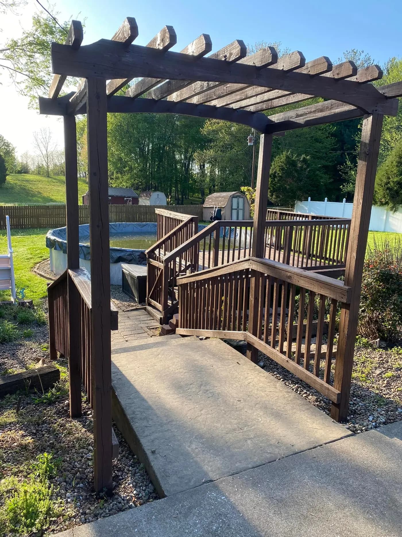 Stained pergola and deck stairs leading to a backyard pool
